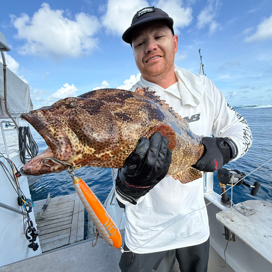 Man holding a large fish caught on a boat with a clear blue sky.
